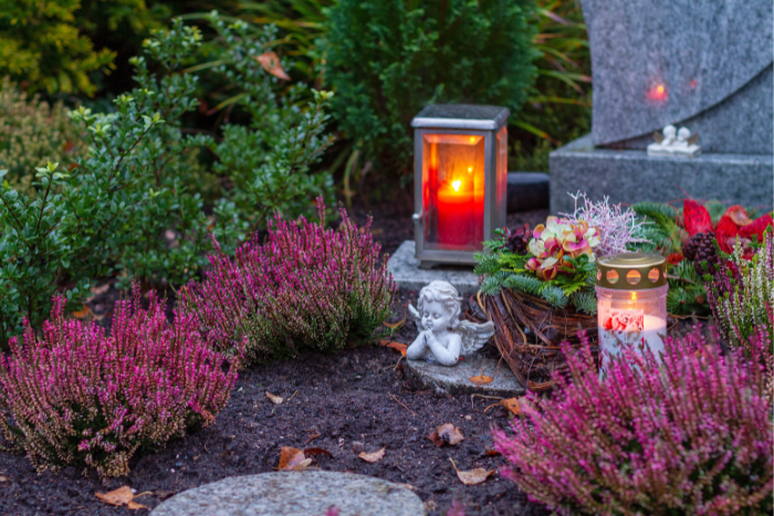 Ein rotes Grablicht leuchtet auf einem bepflanzten Grab.