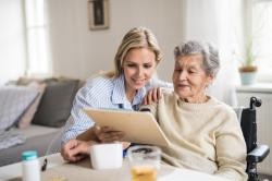 Junge Frau hilft älterer Frau beim Ausfüllen von Formular