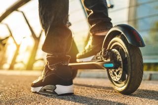 Foto: Adobe Stock Eine Person steht mit einem Fuß auf einem E-Roller