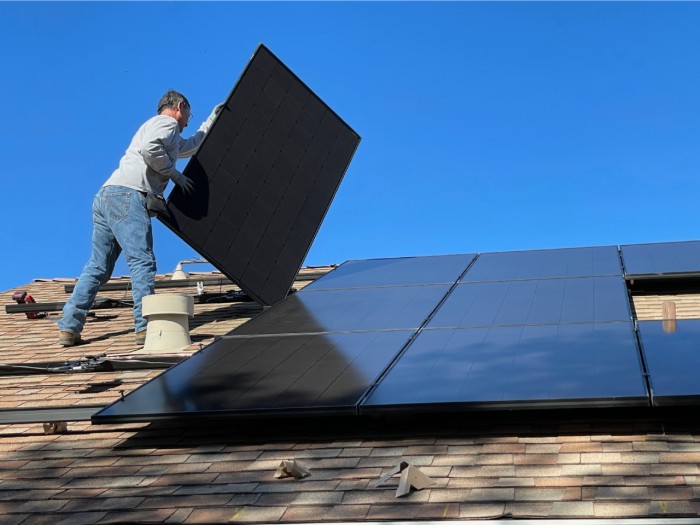 Ein Arbeiter montierrt Solarmodule auf einem Hausdach.