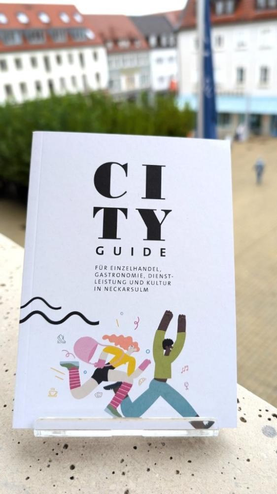 Foto des Cityguides auf einem Fenstersims mit dem Marktplatz im Hintergrund.