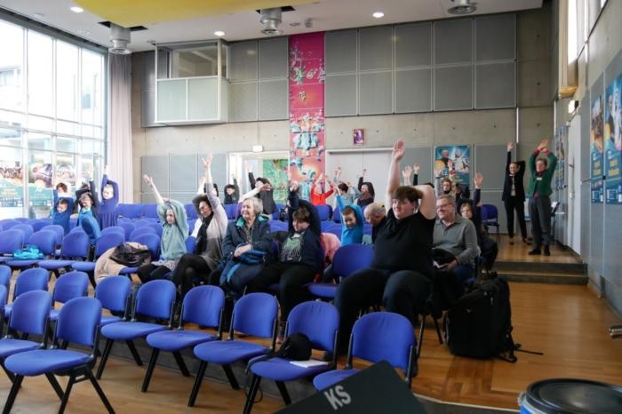 Besucher im Konzertsaal bei einer praktischen Körperübung 