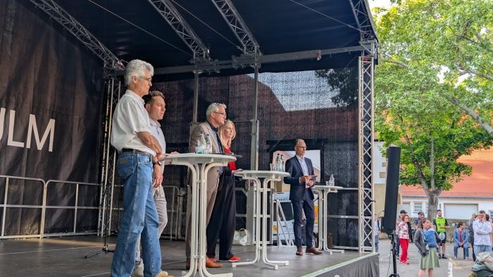Die Vertrauenspersonen und die Vertreter der Stadt stehen auf der Bühne am Schlossplatz.  
