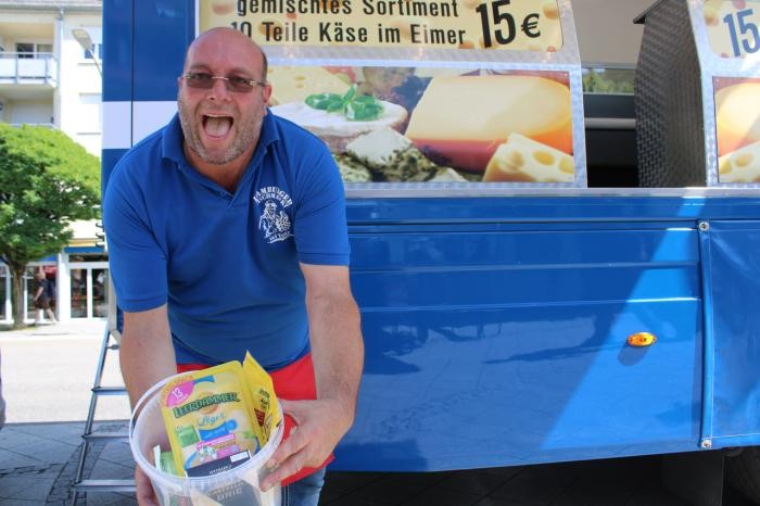 "Käse-Maik" steht vor seinem Verkaufswagen und hält einen Eimer mit Käseprodukten in Händen. Foto: Jobo