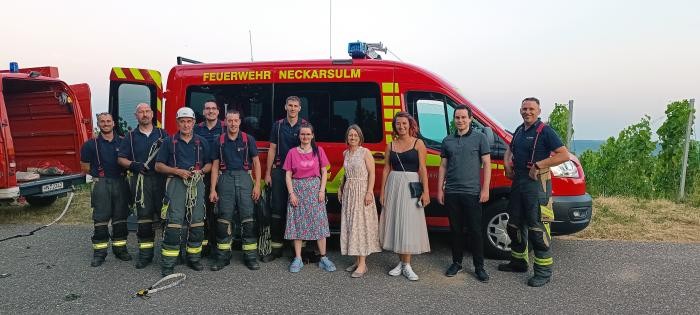 Feuerwehrmänner, drei Frauen und ein Mann stehen vor einem Feuerwehrauto für ein gemeinsames Foto