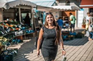 Eine Frau läuft lächelnd über den Wochenmarkt. In ihrer Hand hält sie eine Tasche mit Einkäufen.