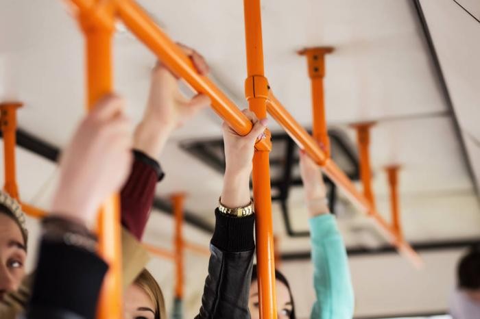 Hände halten sich im Bus an den oberen Griffstangen
