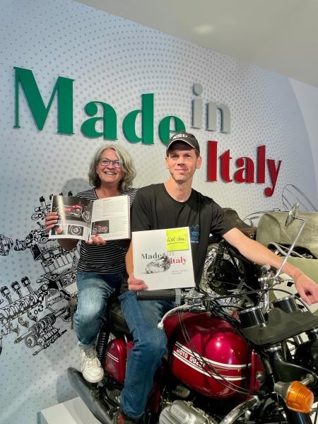 Sven Heimberger und Beate Schick sitzen auf einem Motorrad und präsentieren die Begleitbroschüre.