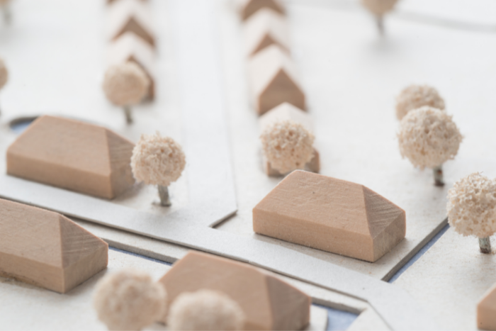 Hölzerne Modelle von Häusern stehen mit Modellbäumchen auf einem Modellplan.