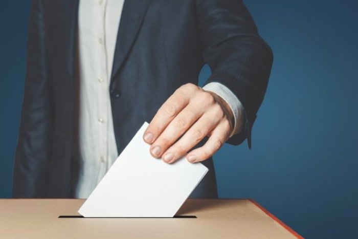 Eine Person steckt einen Wahlumschlag in eine Wahlurne.