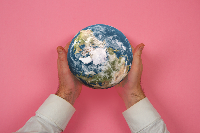 Zwei Hände halten eine Weltkugel vor einem pinkfarbenen Hintergrund.