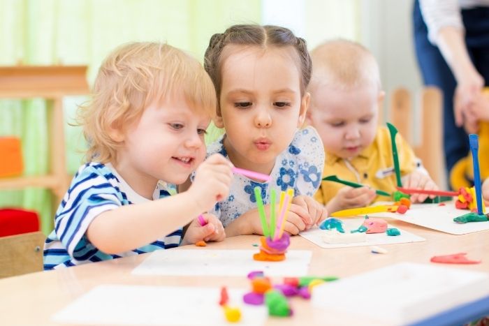 Drei Kinder im Kindergartenalter spielen gemeinsam an einem Tisch mit Knete.