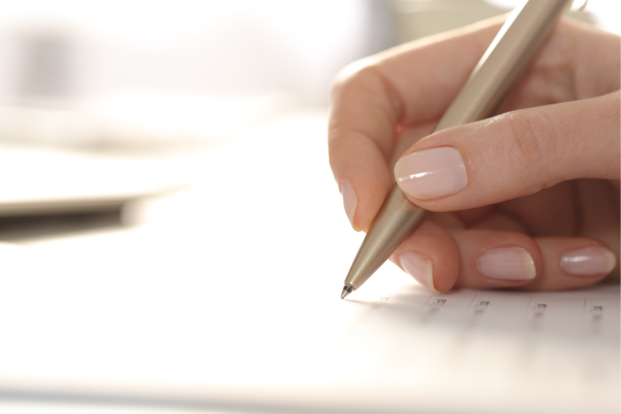 Eine Hand hält einen Stift und schreibt auf einem Dokument. Detailaufnahme.