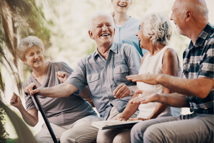 Vier ältere Menschen sitzen beieinander und lachen. Eine ältere Frau steht hinter der Gruppe und lacht mit. 