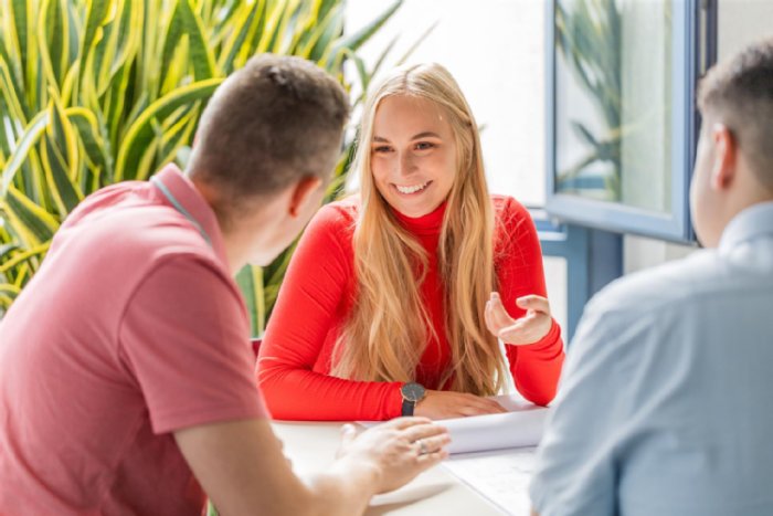 Drei Personen sitzen an einem Tisch mit Unterlagen und unterhalten sich