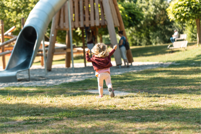 Ein Kind läuft auf einem Spielplatz auf ein Spielgerät zu.