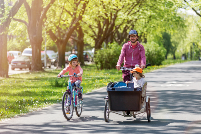 Vater und Töchter fahren mit einem Fahrrad und einem Lastenrad.